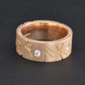 Heavy man’s rose gold ring engraved with runes and set with diamonds in the band.
